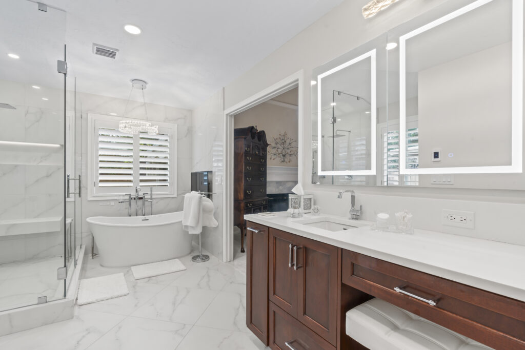 Modern bathroom design featuring a freestanding tub, glass shower enclosure, dual vanities with wood cabinetry, and elegant lighting, showcasing a luxurious remodeling aesthetic by Miss K Kitchen and Bath Remodels in Utah.
