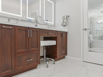 04-DSC04358 Modern bathroom vanity with rich wooden cabinetry, white countertop, and a rolling stool, showcasing sleek mirrors and stylish fixtures, emphasizing design elements for remodeling projects.