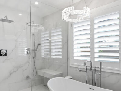 11-DSC04305 Modern bathroom featuring a sleek freestanding tub, elegant chrome fixtures, and a glass shower enclosure, accented by marble walls and stylish plantation shutters, highlighting luxurious design elements for remodeling inspiration.