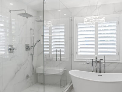 12-DSC04309 Modern bathroom featuring a glass shower enclosure, freestanding bathtub, marble walls, and stylish window shutters, emphasizing luxury and contemporary design in home remodeling.