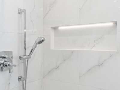 14-DSC04304 Modern shower featuring sleek chrome fixtures, marble-patterned tiles, and a built-in niche with ambient lighting.