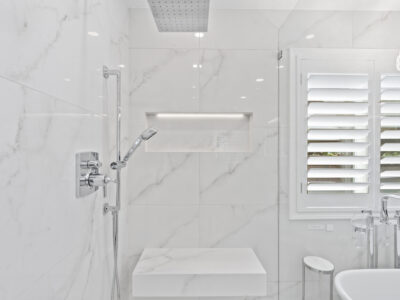 17-DSC04326 Modern bathroom featuring white marble tiles, sleek shower fixtures, and a minimalist design with natural light from a window.