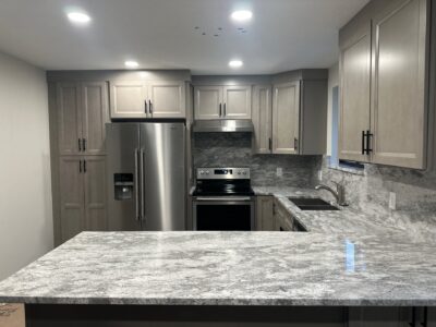 19-Nov 19 2024 12_00am-PQk8 Modern kitchen featuring gray granite countertops, light wood cabinetry, stainless steel appliances, and under-cabinet lighting.