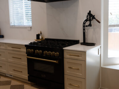 Alyssa10 Modern kitchen featuring a black gas range with gold knobs, white cabinetry, and a marble countertop, emphasizing stylish design for kitchen remodeling.