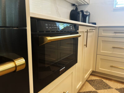 Alyssa2 Modern kitchen featuring a black oven with gold accents, white cabinetry, and a coffee maker, highlighting stylish design elements for remodeling projects.