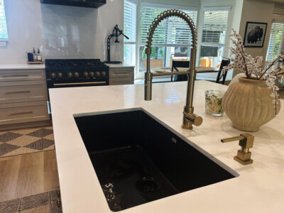 Alyssa3 Modern kitchen countertop with a black sink, stylish gold faucet, and decorative vase, showcasing elegant design elements for remodeling inspiration.