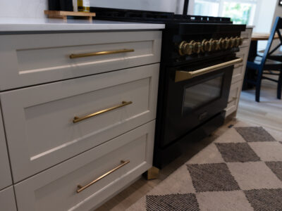 Alyssa5 Modern kitchen cabinetry with sleek white drawers, gold handles, and a black gas range, highlighting design elements for kitchen remodeling.