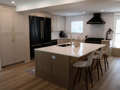 Alyssa6 Modern kitchen featuring a spacious island with white countertop, stylish bar stools, black appliances, and elegant cabinetry, showcasing an inviting design ideal for remodeling and countertop material selection.