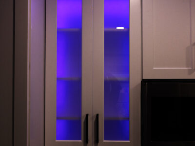 Chris7 Modern kitchen cabinetry with illuminated glass doors featuring purple lighting, showcasing stylish storage solutions for kitchen remodeling projects.
