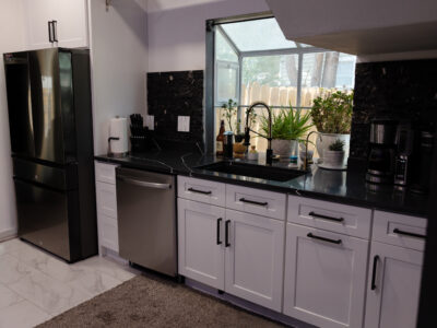 Chris9 Modern kitchen featuring black granite countertops, white cabinetry, stainless steel appliances, and a window with indoor plants, illustrating a stylish and functional remodeling design.