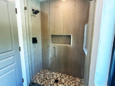 Kristen Modern bathroom shower featuring textured wall tiles, built-in niche, and pebble stone floor, emphasizing contemporary design and functionality for remodeling projects.