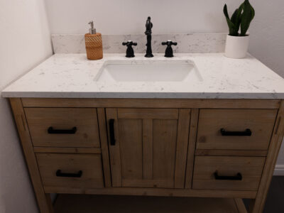 Kristen5 Bathroom vanity with white marble countertop, black faucet, wooden cabinetry, and decorative plant, illustrating modern bathroom design and countertop material options for remodeling.