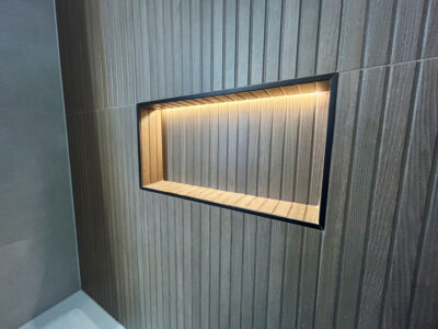 Natale2 Modern bathroom wall niche with horizontal wood paneling and integrated lighting, showcasing a sleek design element for storage and aesthetics in remodeling projects.