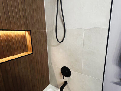Natale5 Modern shower design featuring sleek black fixtures, textured wood paneling, and light-colored tiles, emphasizing luxury and functionality in bathroom remodeling.
