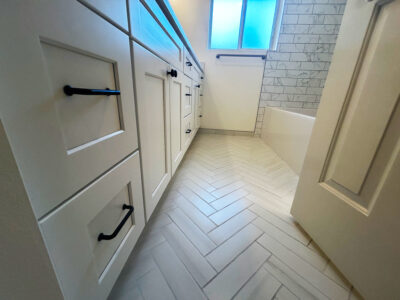 Zack1 Modern bathroom interior featuring white cabinetry with black hardware, herringbone tile flooring, and a window providing natural light, emphasizing a stylish and functional design for remodeling projects.