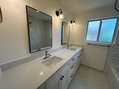 Zack2 Modern bathroom with dual sinks, sleek white countertops, large mirrors, and natural light from a window, showcasing a clean and functional design ideal for remodeling.