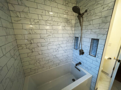 Zack9 Modern bathroom featuring a white bathtub, sleek showerhead, and elegant marble-patterned tile walls, showcasing a stylish and functional remodeling design.